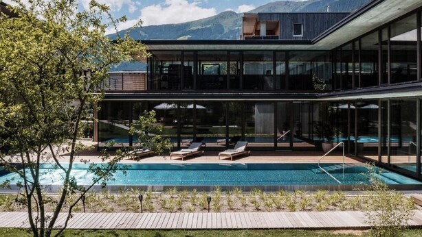 A modern house with a swimming pool, large glass windows, and a view of mountains.