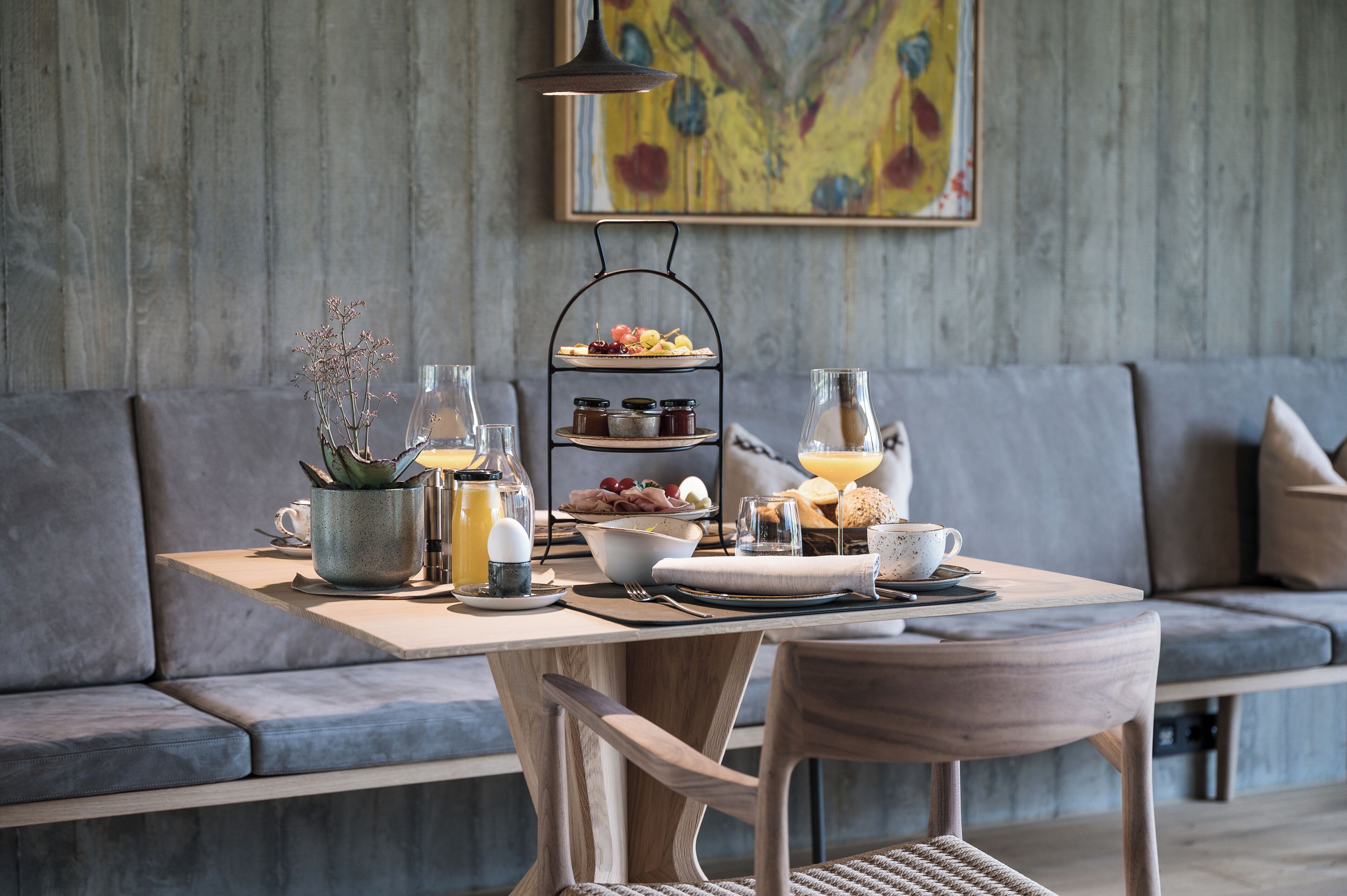 A breakfast setup with a tiered serving tray, a coffee cup, and a vase of dried flowers on a wooden table.