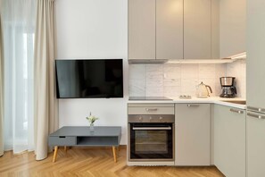 Ett modernt kök med en inbyggd ugn, en kaffebryggare och en platt-TV som är monterad på väggen.