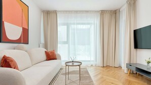 Ein modernes Wohnzimmer mit einer Couch, einem kleinen runden Tisch, einem Fernseher und einem großen Fenster mit Vorhängen.