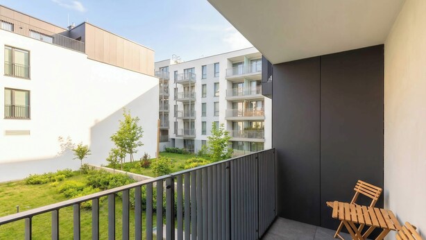 Ein Balkon mit Blick auf einen Innenhof, ein Holzstuhl und ein modernes Gebäude mit Balkonen.