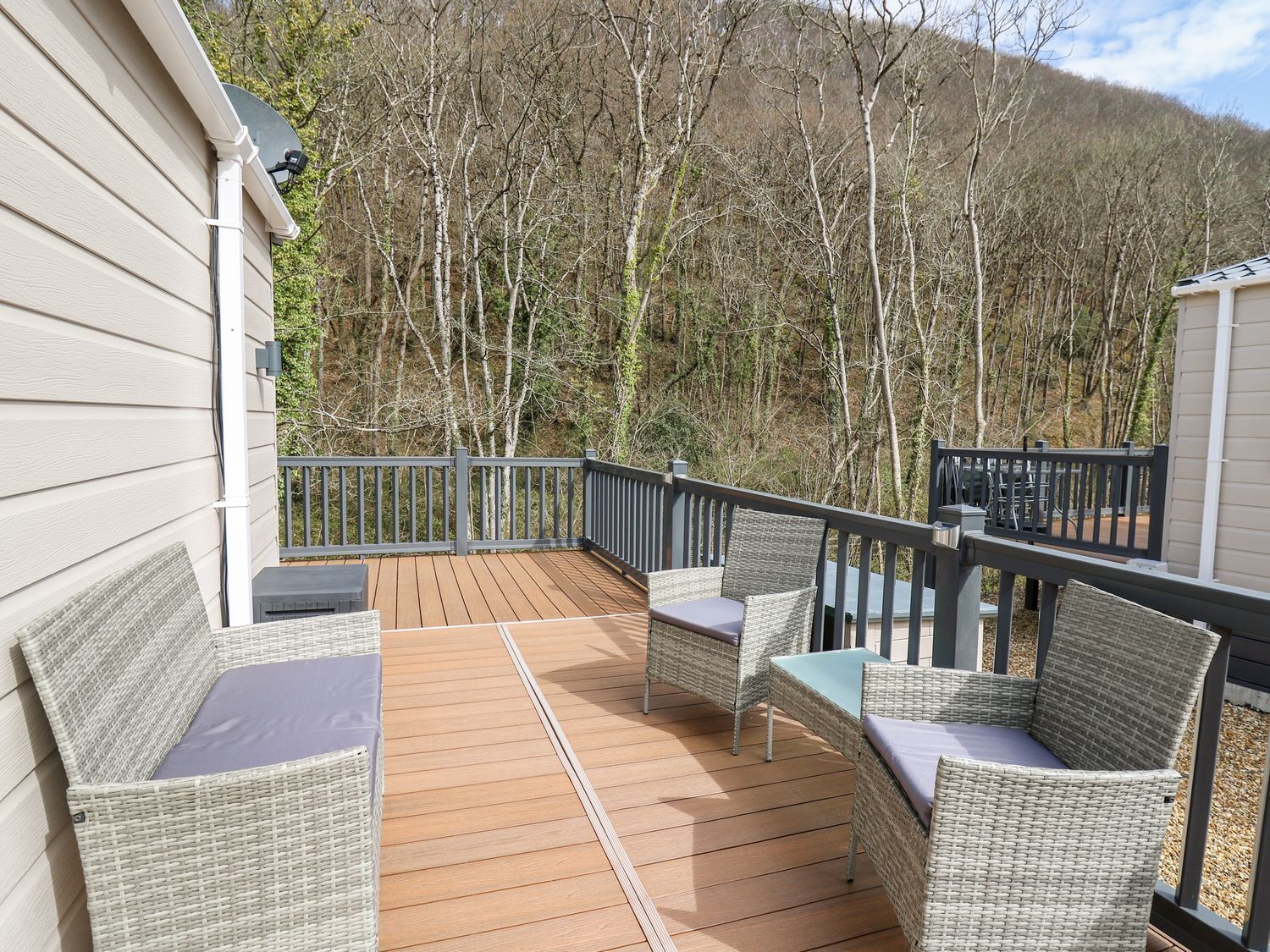 A wooden deck with wicker furniture and a view of a forested hillside.