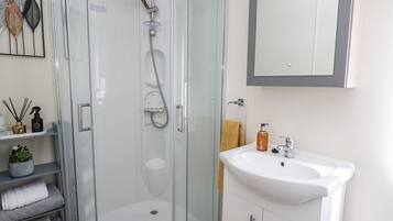 Een moderne badkamer met een douchecabine van glas, een witte wastafel en een handdoekhouder.