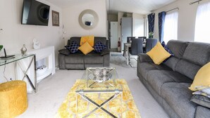 A modern living room with a grey sofa, a coffee table, and a dining area in the background. - 33 Woodpecker Lodge (New Quay)