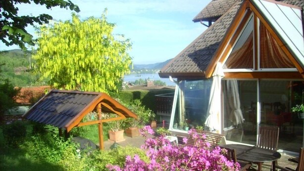 Una casa con techo inclinado, puerta de cristal y jardín con plantas en flor.