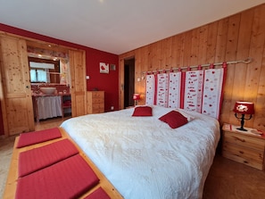 A bedroom with a wooden headboard, a large bed with red pillows, a bedside table with a lamp, and a wooden wardrobe.