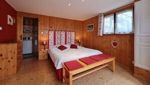 Un dormitorio con paneles de madera, una cama, lámparas de noche, una mesita y un ventanal con cortinas.