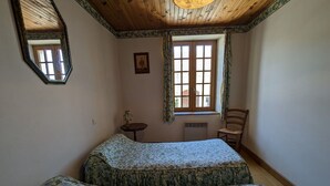 Une chambre avec deux lits, une fenêtre avec des rideaux, une chaise, une petite table et un miroir.