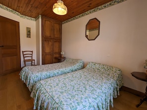 Une chambre avec deux lits, une armoire en bois, une chaise et un miroir au mur.
