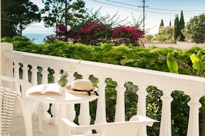 Un balcone bianco con tavolo e sedie, un libro e un cappello di paglia.