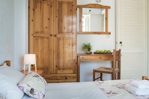 A bedroom with a wooden wardrobe, a bedside table with a lamp, a desk with a mirror, and a chair. - Sunset Beach Apartments (Kefalonia)