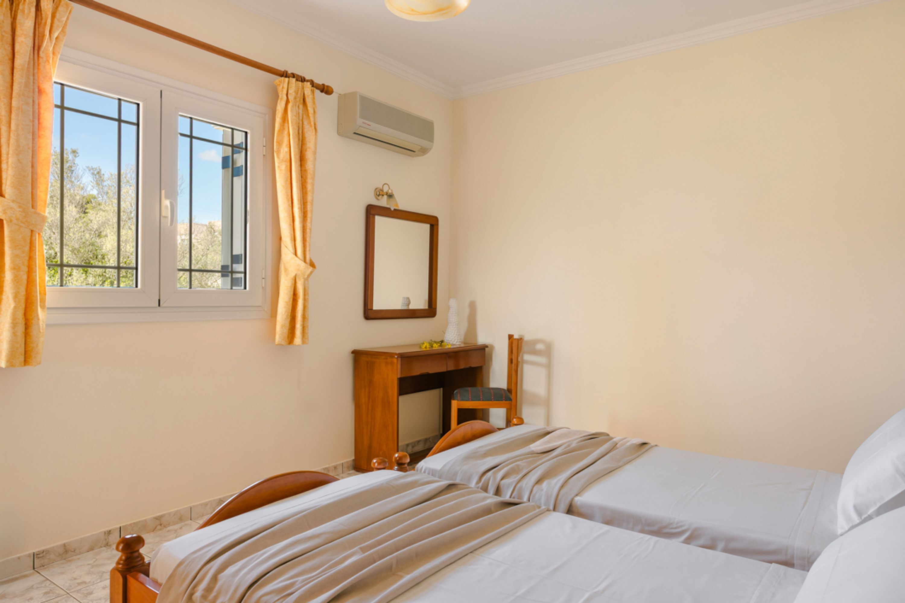 Quarto de hotel com duas camas, uma escrivaninha com cadeira, um espelho e um ar condicionado.