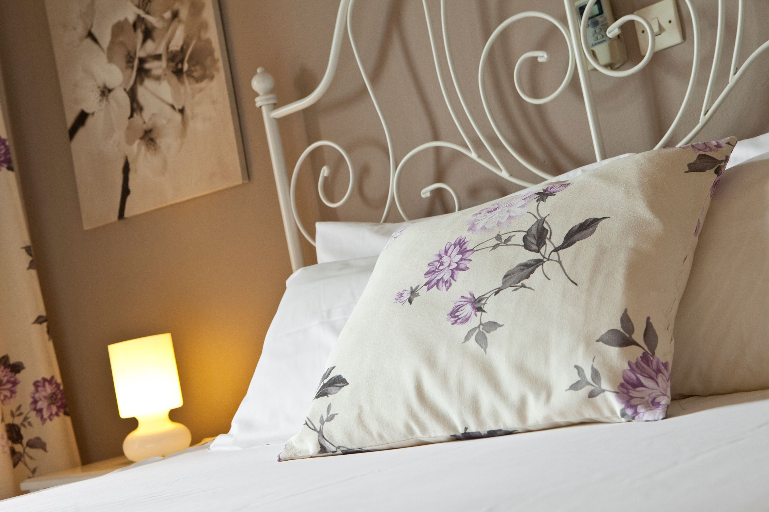 Cama bem arrumada com almofadas florais e cabeceira de metal branca.