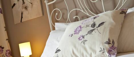 Cama bem arrumada com almofadas florais e cabeceira de metal branca.