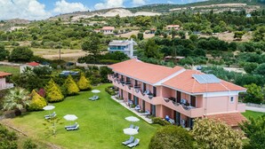 Un hotel de diversos pisos amb teulada vermella, zona de piscina amb gandules i ombrel·les, i un jardí verd i exuberant.