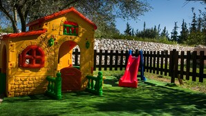 Una zona de jocs amb un tobogan, una casa i espais per pujar.