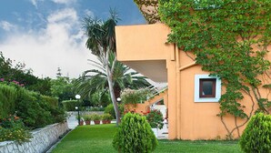 Un jardí ben cuidat amb una paret de pedra, una palmera i un edifici amb teulada i finestra.