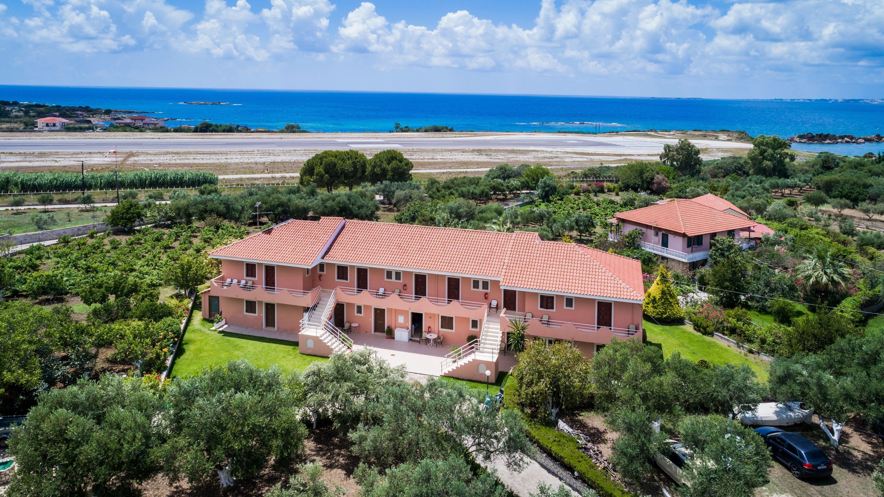 Un edificio de dos pisos con techo de tejas rojas, rodeado de vegetación y vistas al mar.