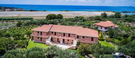 Un edificio de dos pisos con techo de tejas rojas, rodeado de vegetación y vistas al mar.