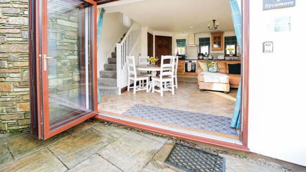 A modern kitchen with a built-in oven, a dining area with a table and chairs, and a staircase leading to an upper level. - Nestled in an elevated position with sweeping views across the Luxulyan Valley. (Penpillick)