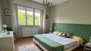 Ein Schlafzimmer mit Bett, Schreibtisch, Stuhl, einem Fenster mit Jalousien und einer Heizung.
