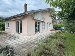 Ein zweistöckiges Haus mit gefliestem Patio, großen Fenstern und einem Auto auf der Auffahrt.