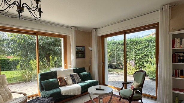 Ein geräumiges Wohnzimmer mit einem grünen Sofa, einem Couchtisch und einem Sessel. Ein Bücherregal mit Büchern und eine Chandelüster sind ebenfalls vorhanden.