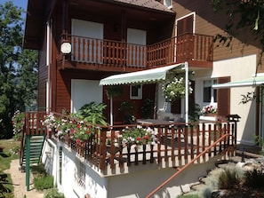 A two-story wooden house with a balcony, outdoor seating, and potted plants.