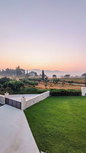Ein angelegter Garten mit einer Steinmauer, einem gepflasterten Bereich und Blick auf entfernte Bäume und Hügel.