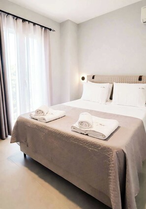 Une chambre d’hôtel avec un lit, deux serviettes enroulées, une tête de lit et une fenêtre avec des rideaux.