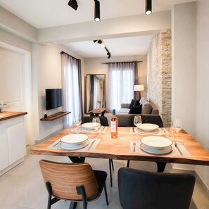 Een eetgedeelte met een houten tafel voor vier personen, een bank, een televisie en een stenen muur.