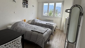 Een slaapkamer met twee bedden, een bureau, een spiegel en een raam met uitzicht op de bergen.