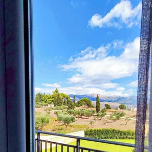 Ein Balkon mit Blick auf eine grüne Landschaft, Bäume und ferne Berge.