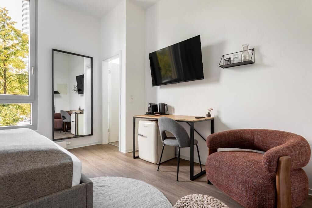 A modern hotel room with a large bed, a desk with a computer, a TV mounted on the wall, and a chair.