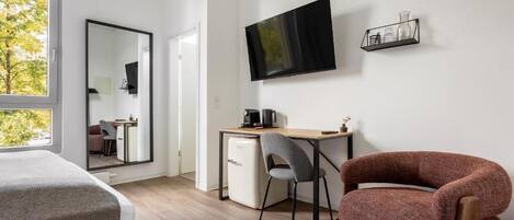 A modern hotel room with a large bed, a desk with a computer, a TV mounted on the wall, and a chair.