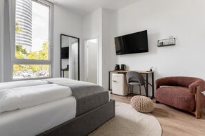 Ein modernes Hotelzimmer mit Bett, Schreibtisch, Stuhl, Fernseher und Blick auf ein Gebäude.
