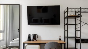 Ein modernes Hotelzimmer mit einem Bett, einem Schreibtisch mit Computer, einem Fernseher und einer kleinen Ablage mit Gegenständen.