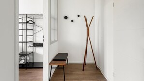 Ein Flur mit einer Bank, einem Ventilator, einem schwarzen Regal und einem an der Wand befestigten Garderobenhaken.