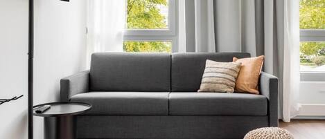 A modern living room with a grey sofa, a round ottoman, and a small black side table.