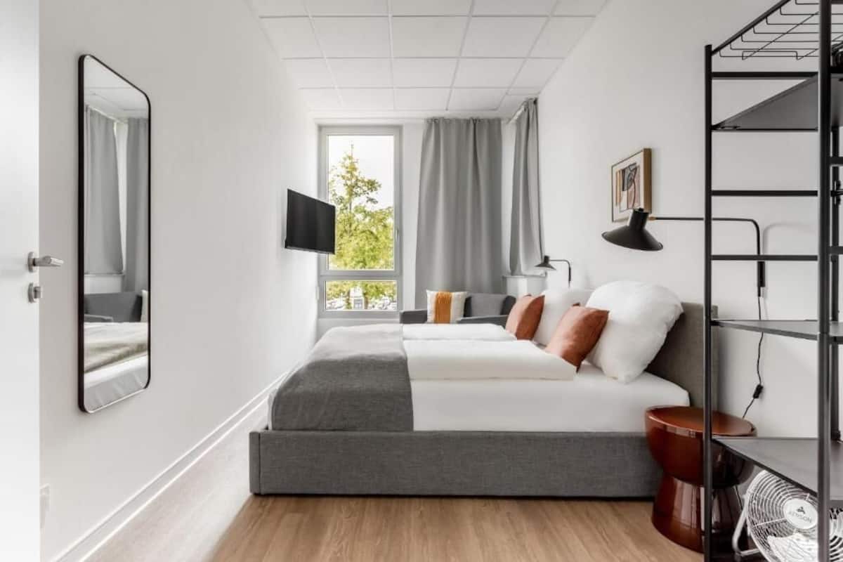 A modern bedroom with a large bed, a TV, a window with curtains, and a bookshelf.