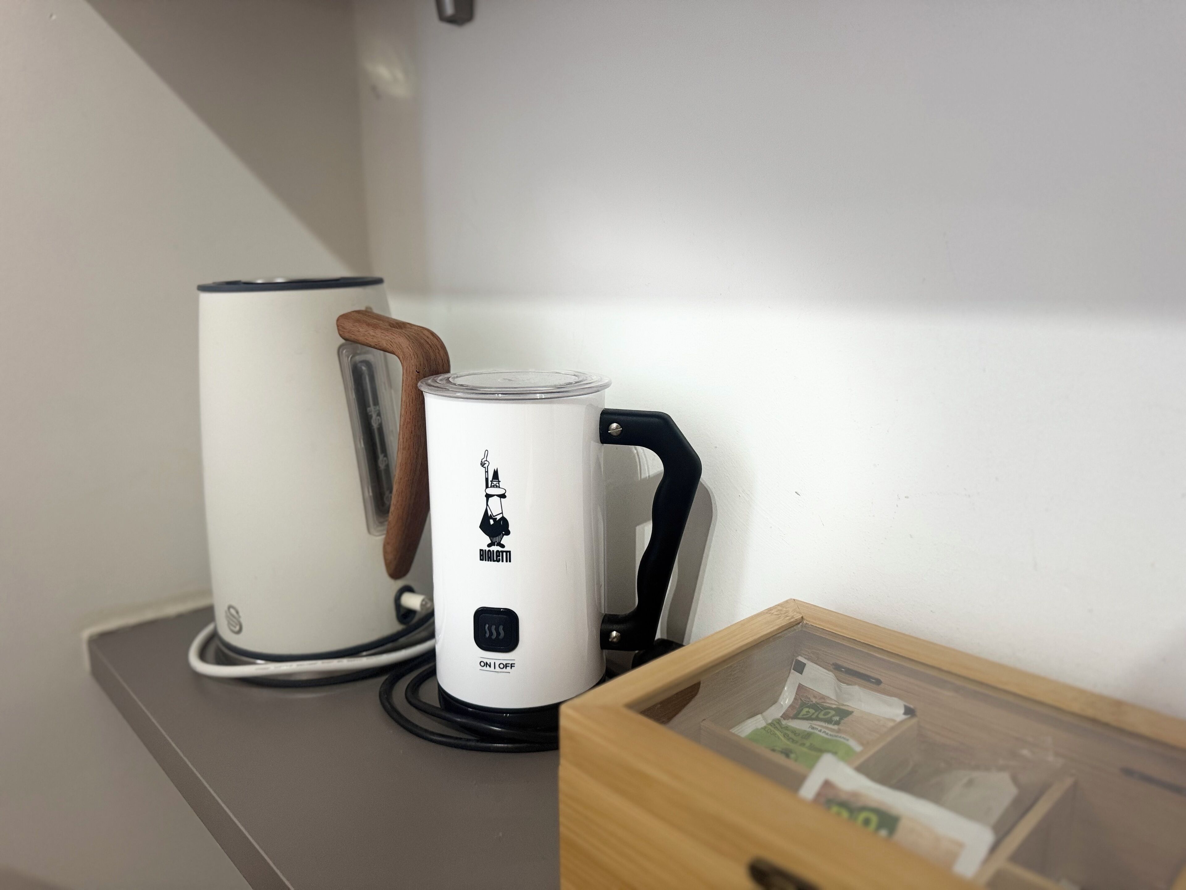A kitchen with a coffee maker, a kettle, and a wooden box containing papers.