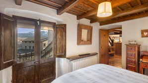 Een slaapkamer met een groot bed, houten balken in het plafond, een raam met uitzicht op gebouwen en bergen, en een radiator.