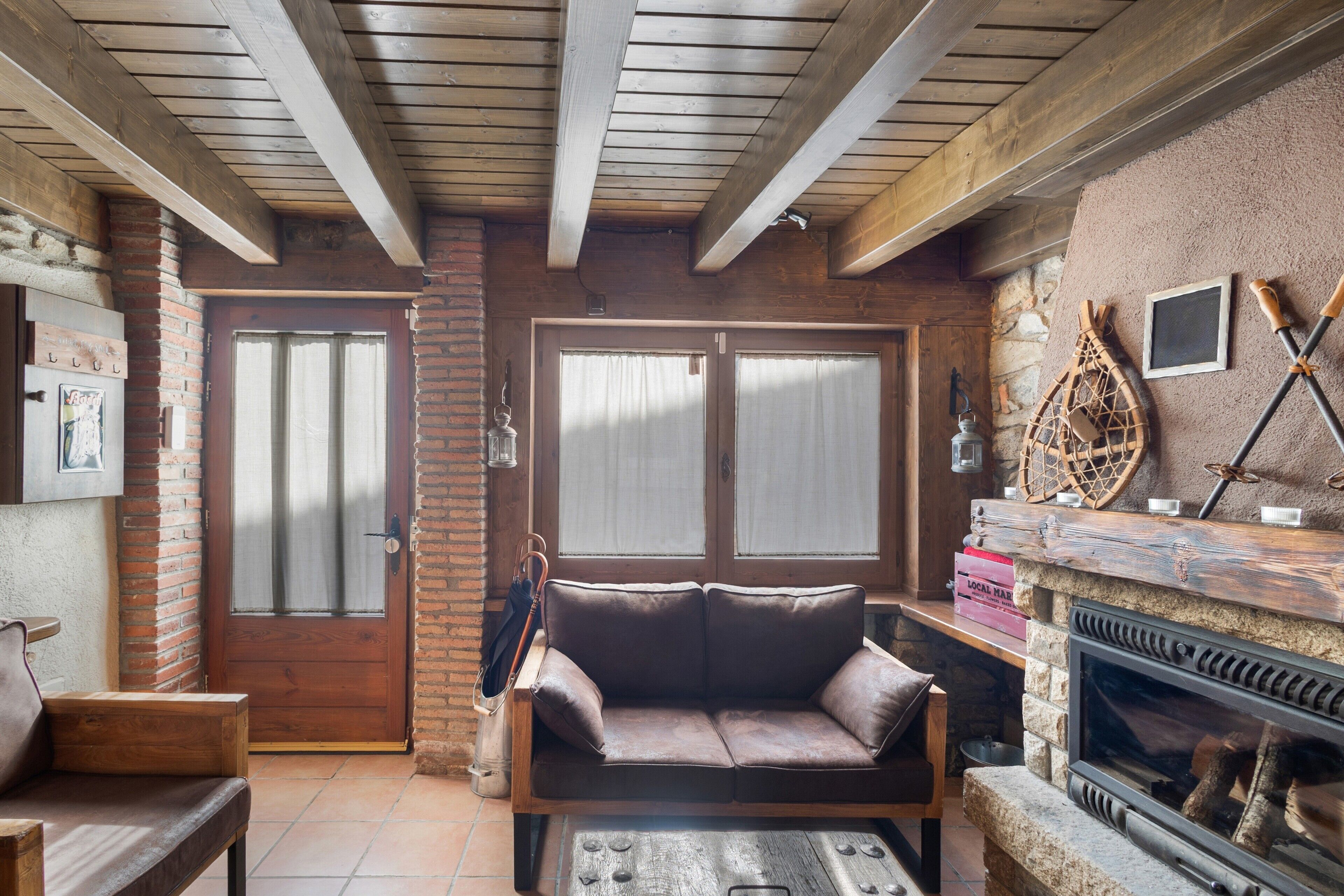 A cozy living room with a fireplace, wooden beams, a sofa, and a door with frosted glass panels.