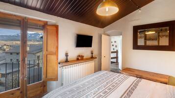 A bedroom with a bed, a mounted TV, a wooden ceiling, and a view of the outside.
