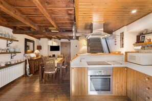 A kitchen with wooden beams, a stove, a microwave, and a dining area with chairs and a table.
