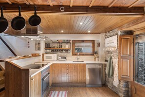 A kitchen with wooden cabinets, stainless steel appliances, and a stone wall.