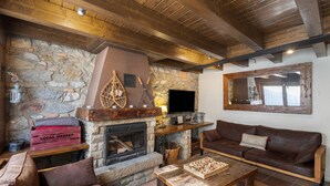 Een rustiek interieur met een stenen open haard, houten balken, een leren bank en een flatscreen televisie.
