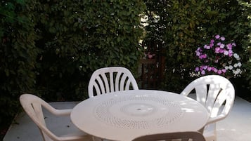 Une table ronde entourée de quatre chaises, le tout bordé d’une haie et d’une clôture en bois.