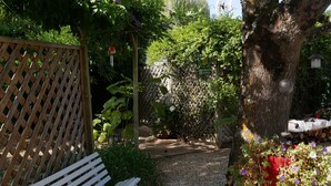 Un jardín con un banco de madera, un sendero de grava y diversas plantas y flores.