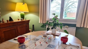 Una mesa de comedor con individuales, vasos rojos y un vaso. Una lámpara y una planta están en la pared.